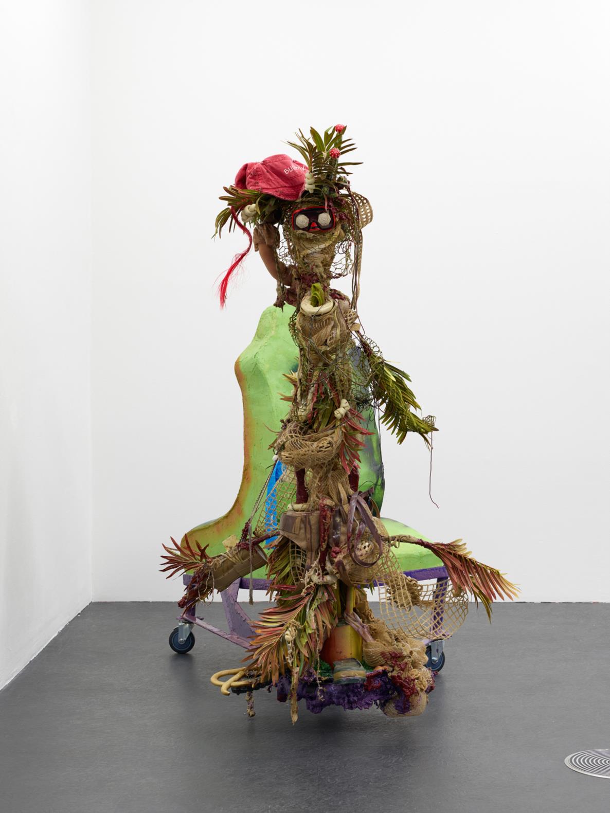 LIZZIE FITCH/RYAN TRECARTIN: Freedom Wake, 2015 Zip ties, ‘S-binder’ clips, plastic clips, metal pipe, cord locks, red wine, denim show, key ring, denim fabric, denim button-down shirt, denim hip-hugger skinny jeans, polyester rope, acrylic paint, spray paint, epoxy, plastic, foam, dog toy penguin, plastic ring trash, leather dog collar, denim hat, burlap basket, dolly, underwear, staples, screws, wood, plastic measuring cups, wire, ‘USA’ scarf, bandana, backpack, paper, decorative craft paper, alphabet stickers, ribbon, thread, stuffing, safety pins, sewing pins, tomato garden stake, sea punk wig, wig, boat bungee ‘airhead’, casters, steel, decoy duck, feathers, ‘plastic-dip’ rubber coating, metal, ‘aaa automobile club of southern California’ stickers